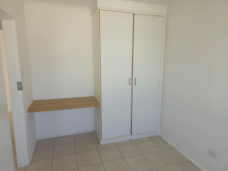 A clean, empty bedroom featuring neutral tiled flooring, a built-in wardrobe, and a convenient integrated desk space.