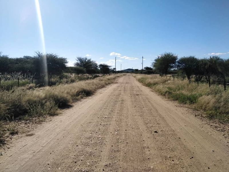 A view of a dirt access road leading through the vacant residential land, bordered by wire fencing and native vegetation.