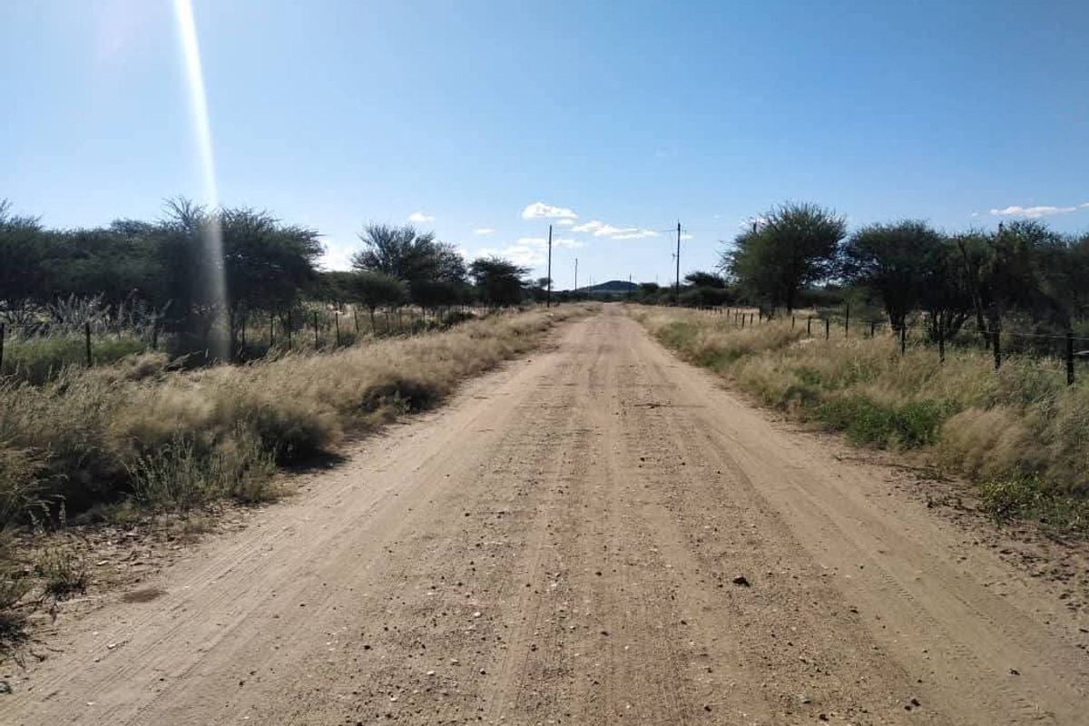 A view of a dirt access road leading through the vacant residential land, bordered by wire fencing and native vegetation.