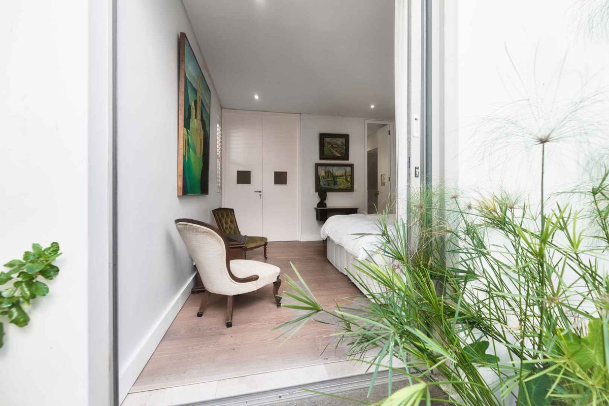 A view from an outdoor area into a bedroom featuring light timber flooring, recessed ceiling lighting, and built-in wardrobe cabinetry.