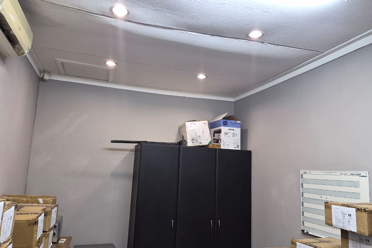 A functional office space featuring recessed ceiling lighting and a wall-mounted air conditioning unit, currently utilized for storage.