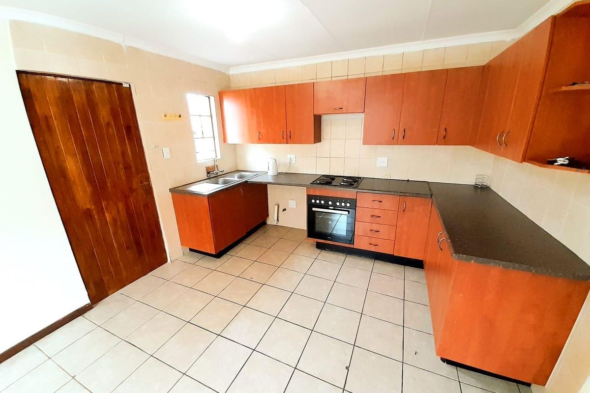 A functional kitchen featuring wooden cabinetry, dark laminate countertops, a built-in oven and hob, and tiled flooring.