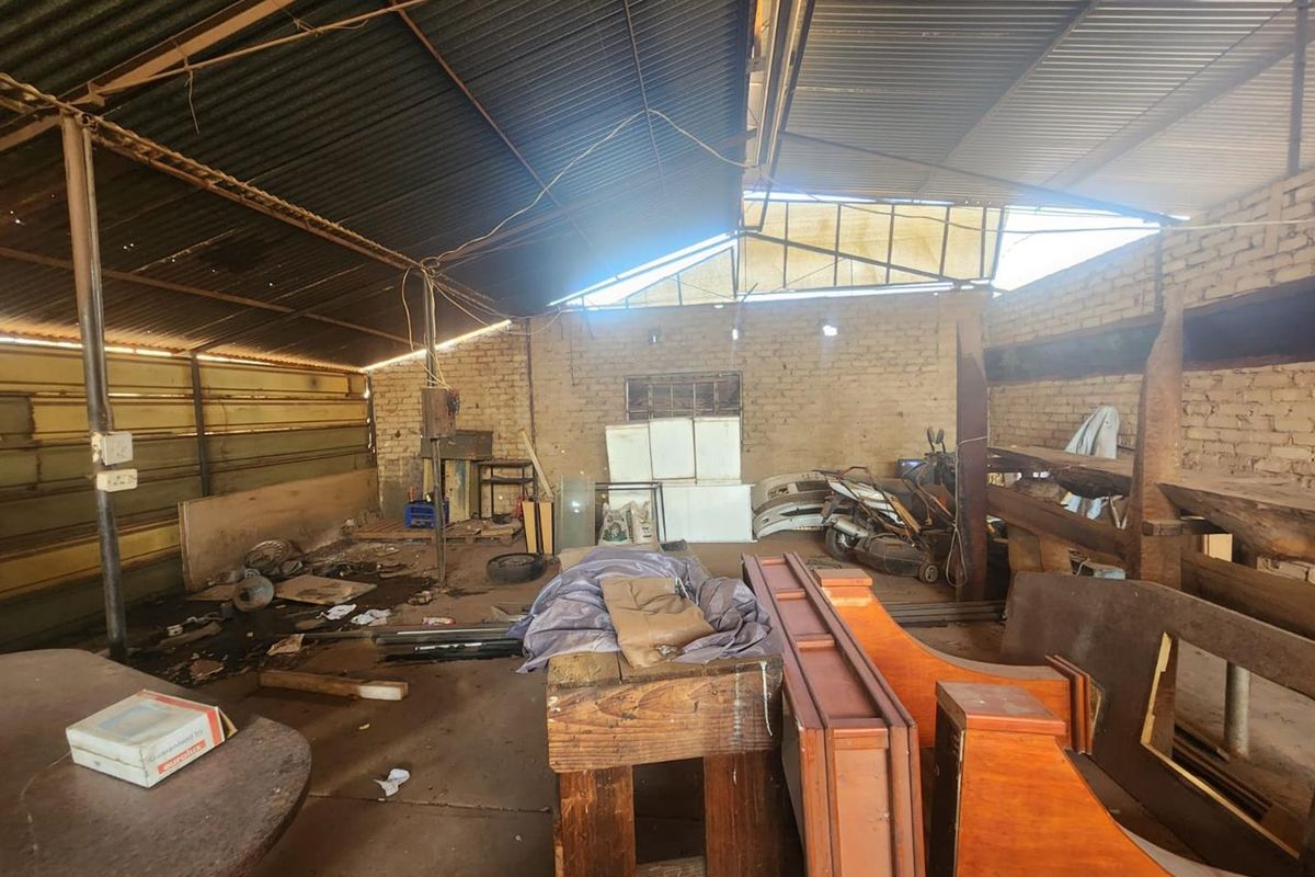 A large, industrial-style utility space featuring exposed brick walls, a corrugated metal roof, and concrete flooring, suitable for storage or workshop conversion.