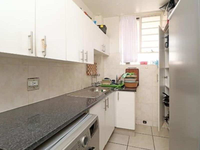 Compact kitchen featuring granite countertops, white built-in cabinetry, tiled backsplash, and tiled flooring with a functional layout.