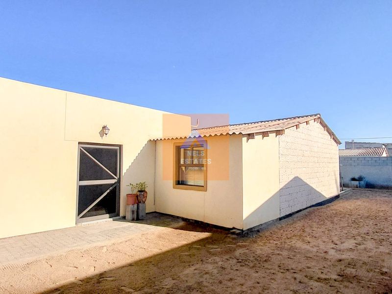Rear view of the property featuring a paved patio area, security screen door, and an unfinished masonry wall section.