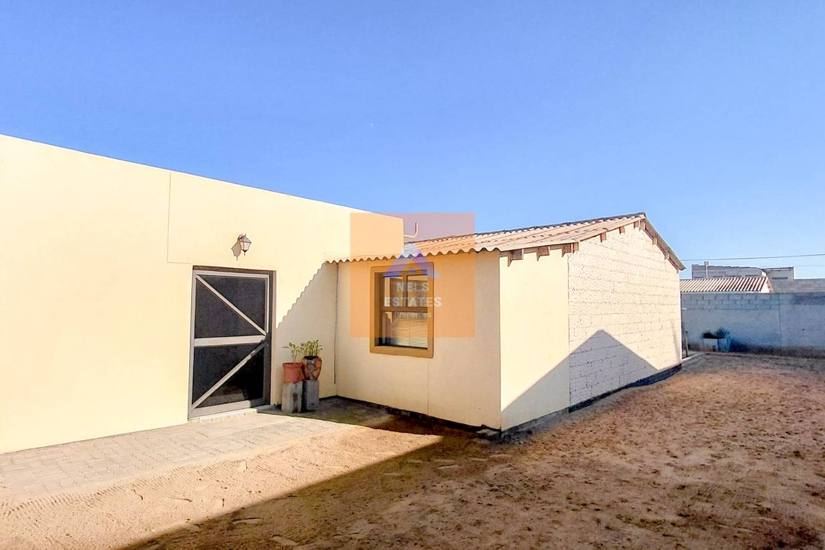 Rear view of the property featuring a paved patio area, security screen door, and an unfinished masonry wall section.