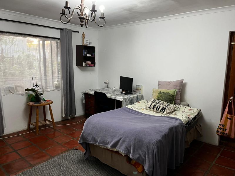 A bedroom featuring traditional terracotta floor tiles, a classic wrought iron chandelier, and neutral wall finishes, offering a functional space with potential for modernization.