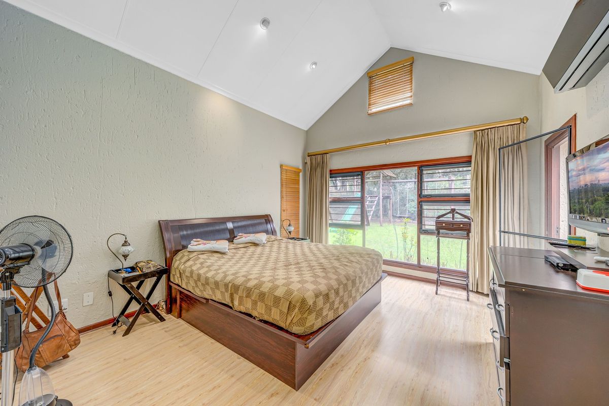 Spacious bedroom featuring a high vaulted ceiling, laminate flooring, and large windows providing natural light and garden views.