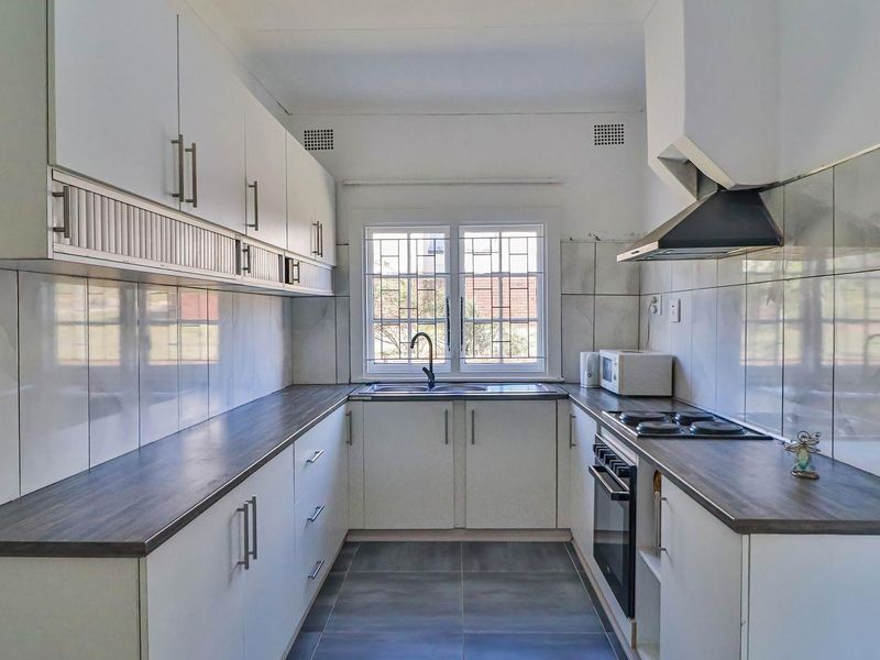 A functional galley-style kitchen featuring white cabinetry, dark laminate countertops, built-in oven, hob, extractor fan, and tiled finishes throughout.