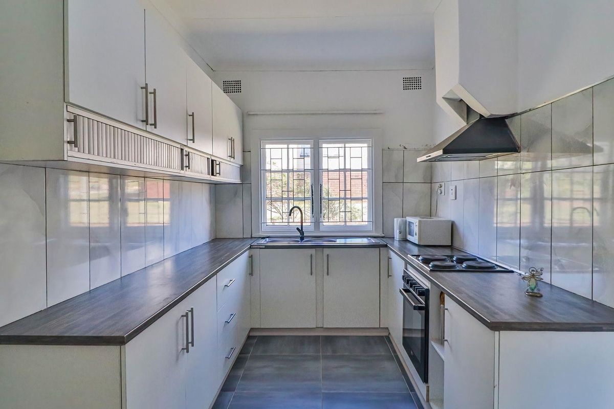 A functional galley-style kitchen featuring white cabinetry, dark laminate countertops, built-in oven, hob, extractor fan, and tiled finishes throughout.