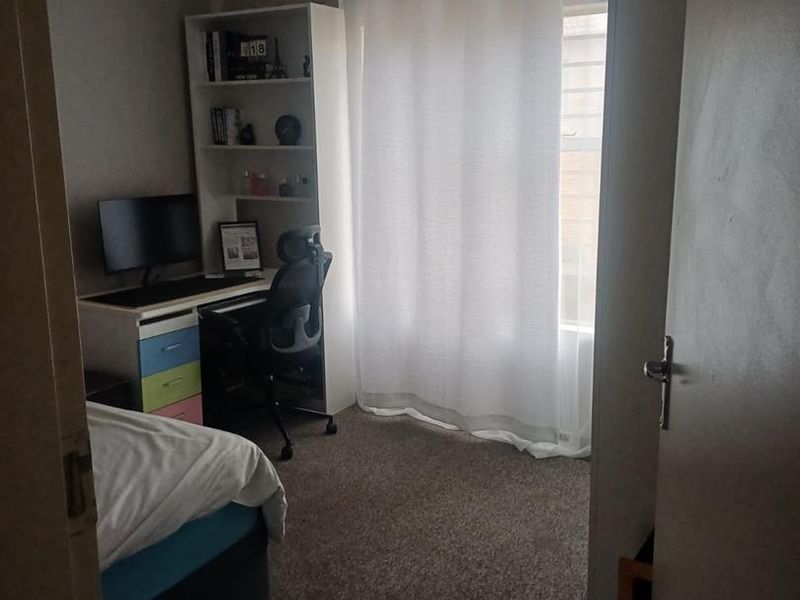 A standard bedroom featuring carpeted flooring, a ceiling light fixture, and a window with curtain rod.