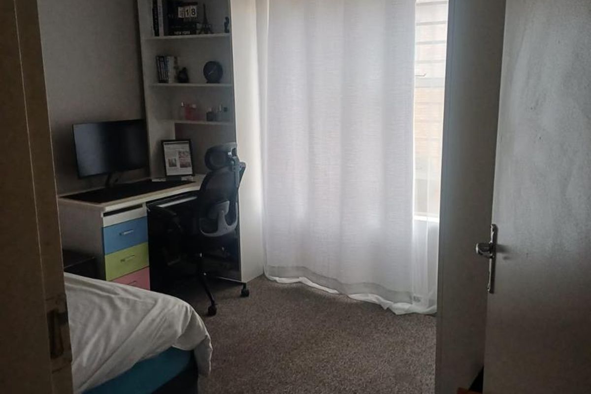 A standard bedroom featuring carpeted flooring, a ceiling light fixture, and a window with curtain rod.