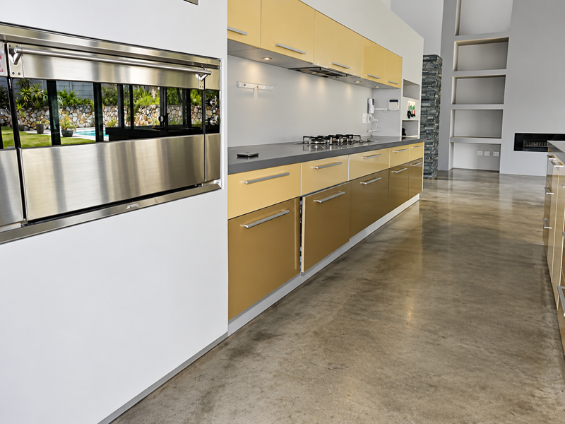 Modern kitchen featuring two-tone cabinetry, built-in Smeg oven, gas hob, and polished concrete floors, flowing into an open-plan living area with a fireplace.
