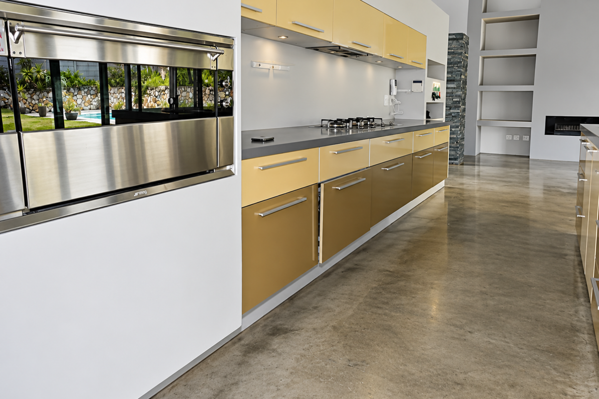 Modern kitchen featuring two-tone cabinetry, built-in Smeg oven, gas hob, and polished concrete floors, flowing into an open-plan living area with a fireplace.