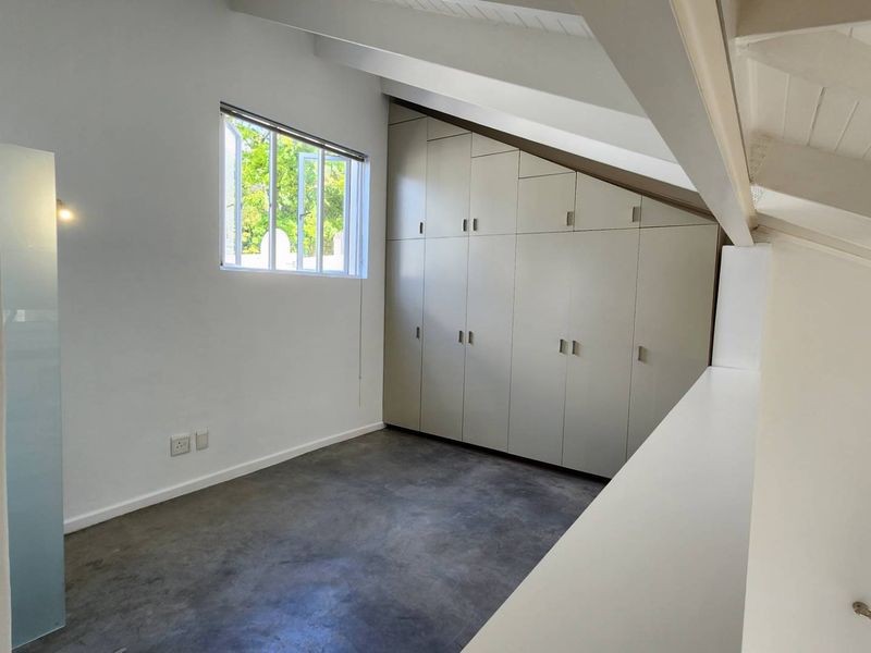 A bright, empty bedroom featuring polished concrete floors, built-in floor-to-ceiling cupboards, and exposed white rafters under a pitched ceiling.