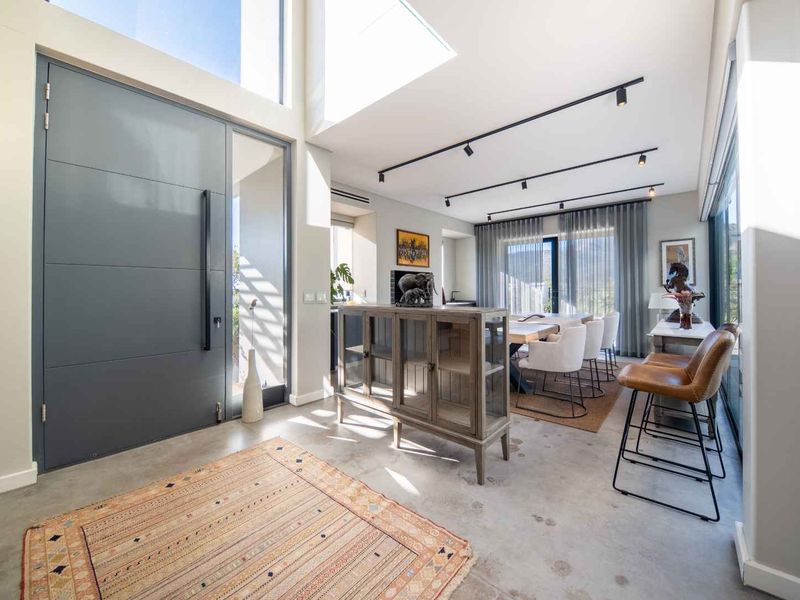 Modern open-plan living area featuring polished concrete floors, high ceilings with skylights, track lighting, and a large contemporary pivot entrance door.