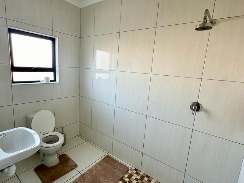 A clean, modern bathroom featuring neutral wall tiles, a walk-in shower area with mosaic floor detailing, a toilet, and a washbasin.