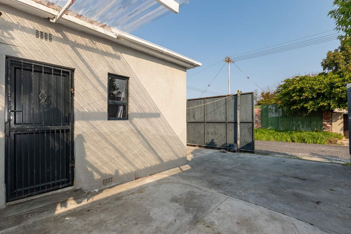 Exterior view of the property showing a concrete paved area, a side entrance with a security gate, and a large metal driveway gate.