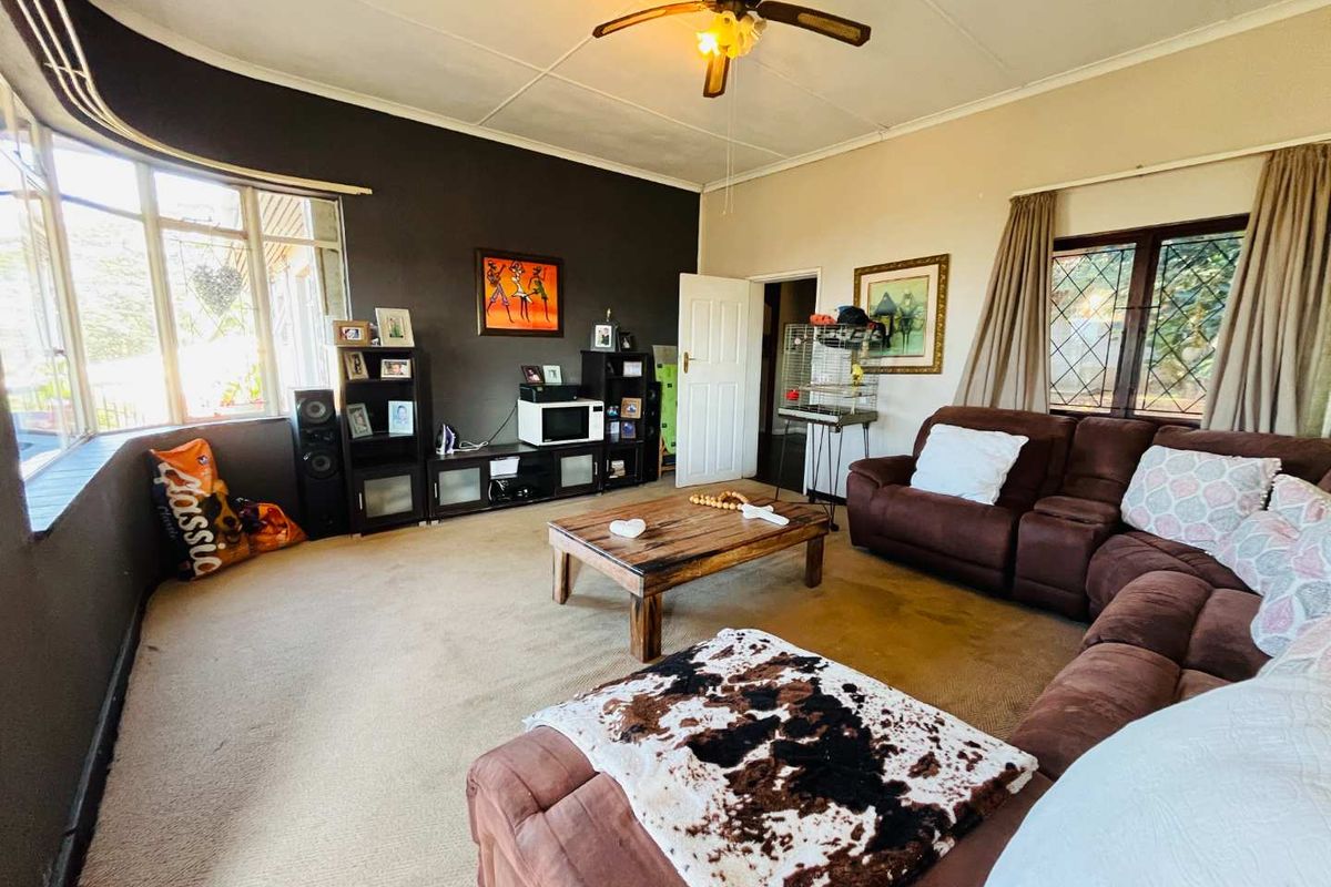 A spacious living room featuring a large bay window, ceiling fan, and neutral wall tones, offering a comfortable and functional family living space.