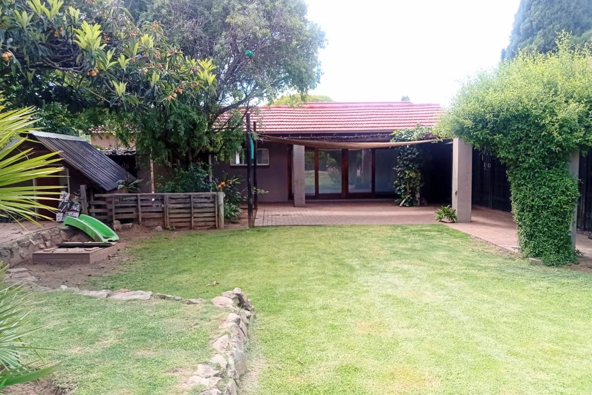 A spacious rear garden featuring a well-maintained lawn, a paved patio area with a shade sail, and established trees.