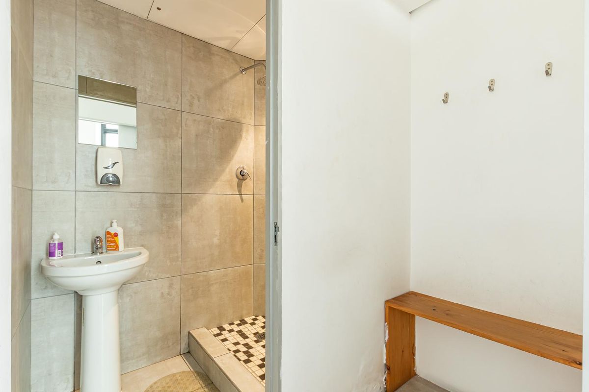 A functional bathroom featuring a pedestal basin, tiled shower enclosure with mosaic floor detail, and an adjacent small dressing or utility area.
