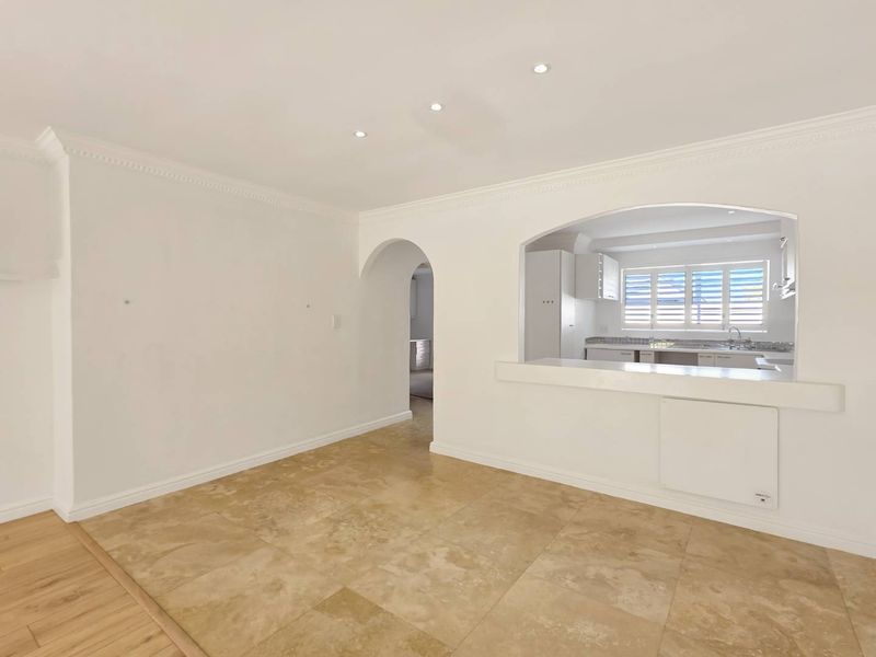 Bright open-plan living area featuring stone flooring, elegant archways, and a convenient pass-through window connecting to the kitchen space.