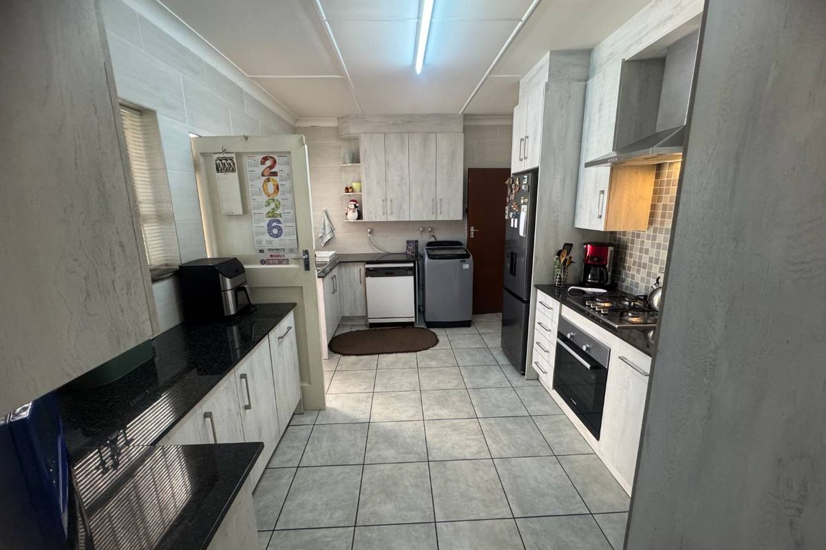 Functional kitchen featuring light wood-grain cabinetry, black granite countertops, built-in oven, gas hob, and integrated laundry space with tiled flooring.