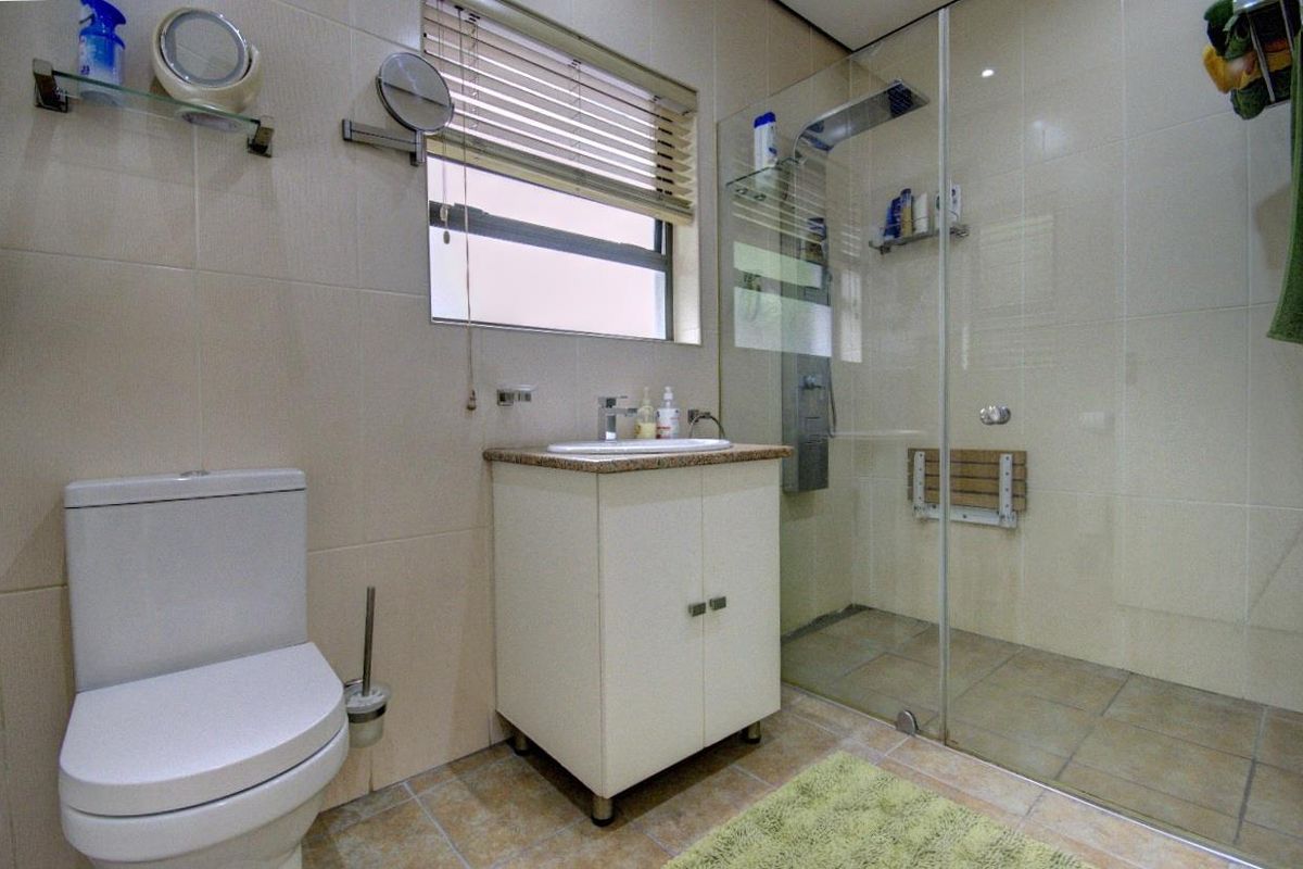 A functional bathroom featuring a walk-in shower with glass enclosure, a vanity basin, and a toilet with neutral wall tiling.