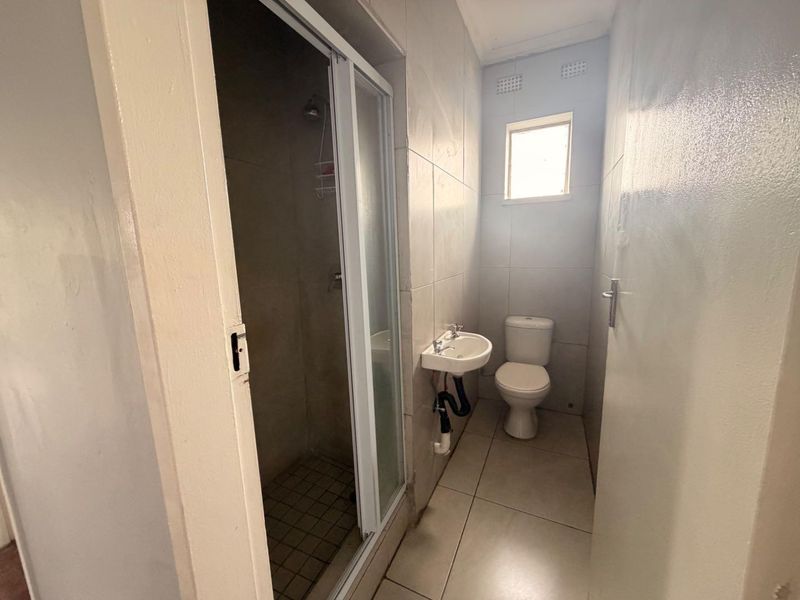 A functional bathroom featuring a shower enclosure, wall-mounted basin, and toilet with tiled finishes throughout.