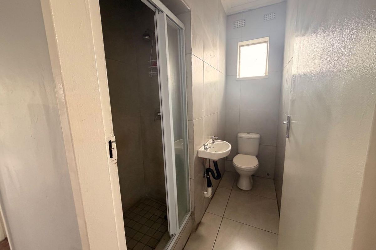 A functional bathroom featuring a shower enclosure, wall-mounted basin, and toilet with tiled finishes throughout.