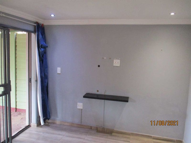 A simple living area featuring tiled floors, recessed lighting, and a sliding door leading to the exterior, with a wall-mounted shelf and electrical points.