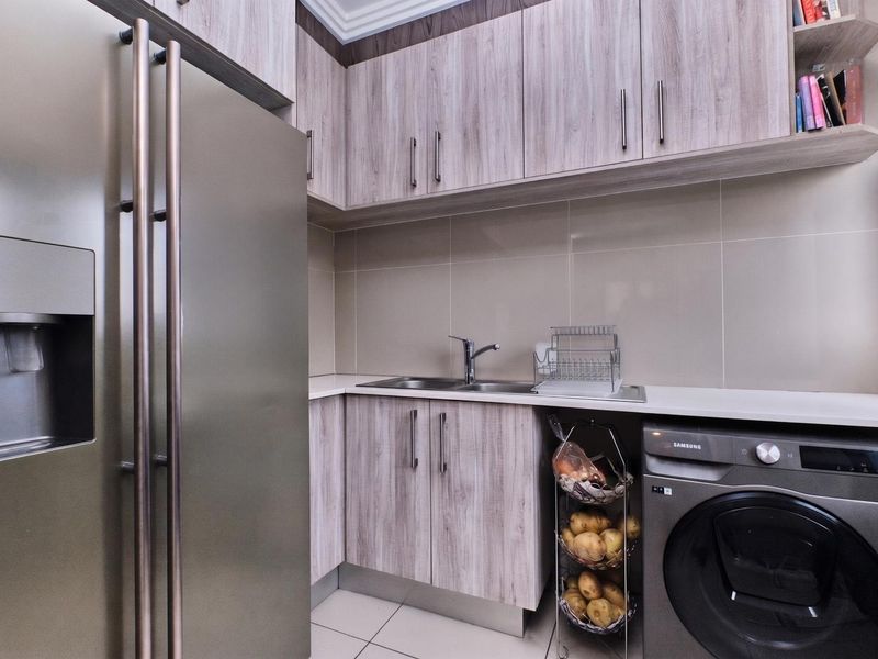 A functional scullery featuring wood-look cabinetry, a stainless steel sink with mixer tap, tiled backsplash, and dedicated space for laundry appliances.