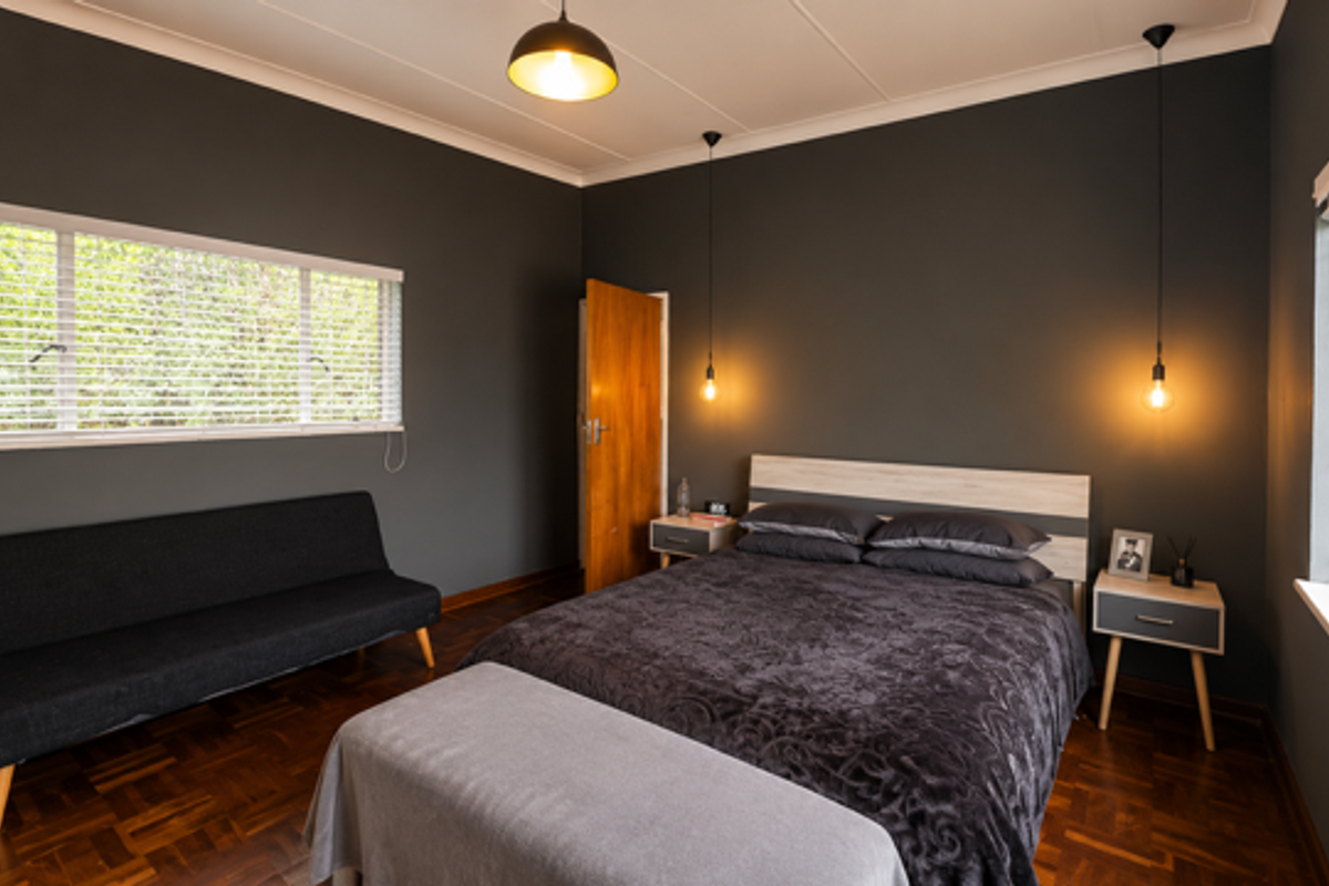 A well-maintained bedroom featuring dark painted walls, parquet flooring, large windows with blinds, and modern pendant lighting.