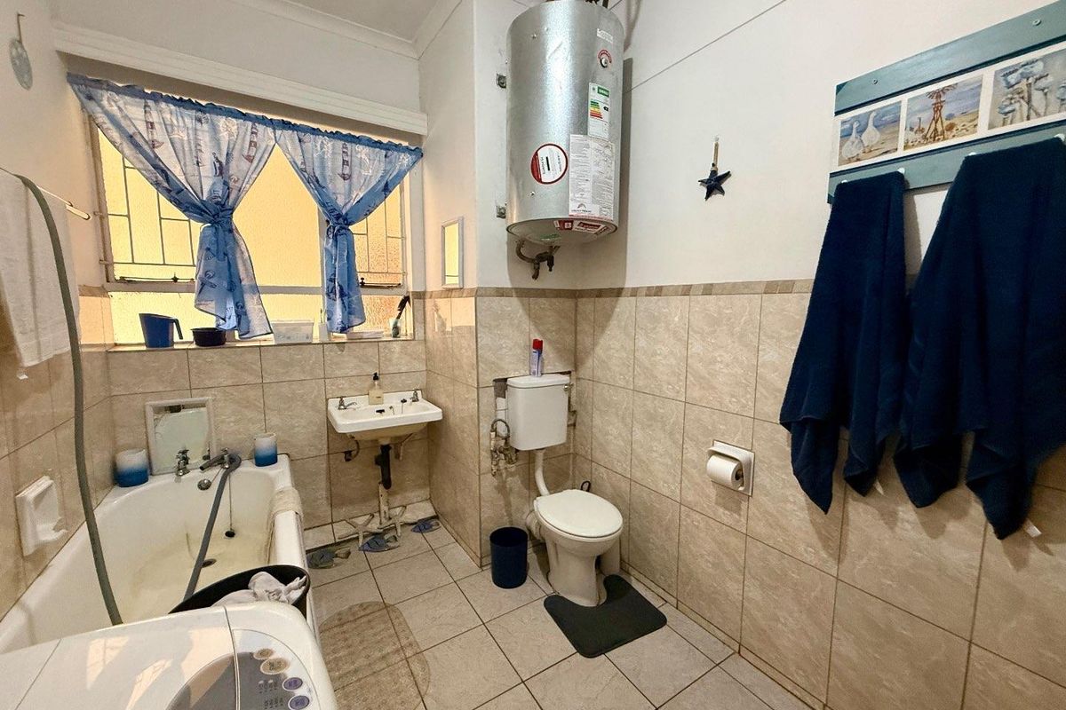 A functional bathroom featuring a bathtub, wall-mounted basin, toilet, and an exposed electric water heater unit.