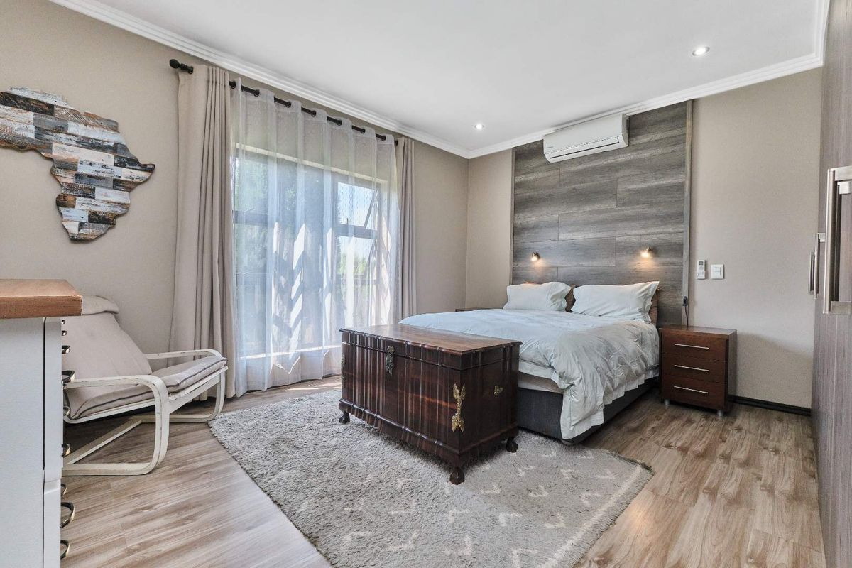 A well-maintained bedroom featuring wood-look laminate flooring, a timber-look feature wall with integrated lighting, and a split-system air conditioner.
