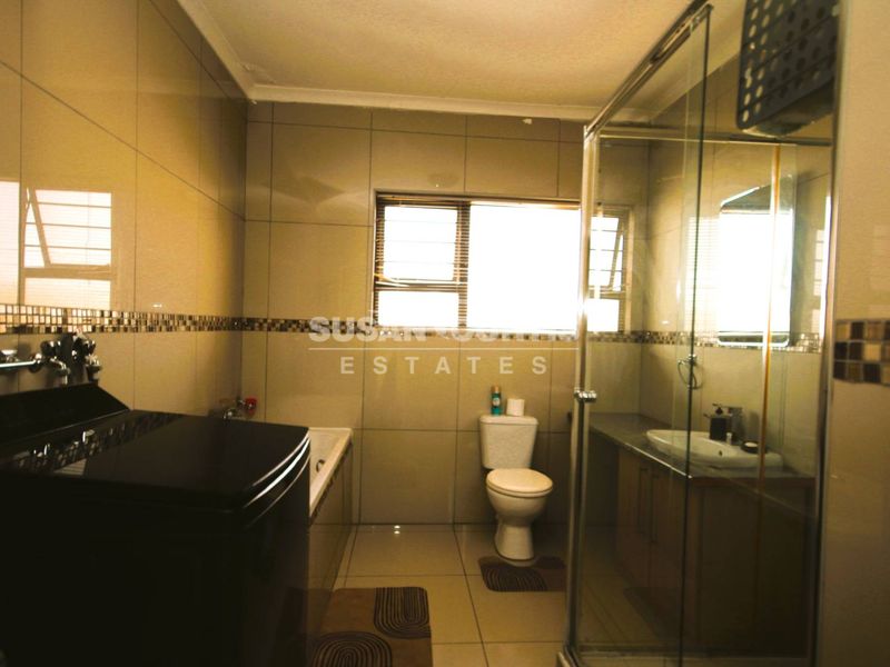 A functional bathroom featuring a shower enclosure, built-in vanity with basin, bathtub, and tiled finishes throughout.