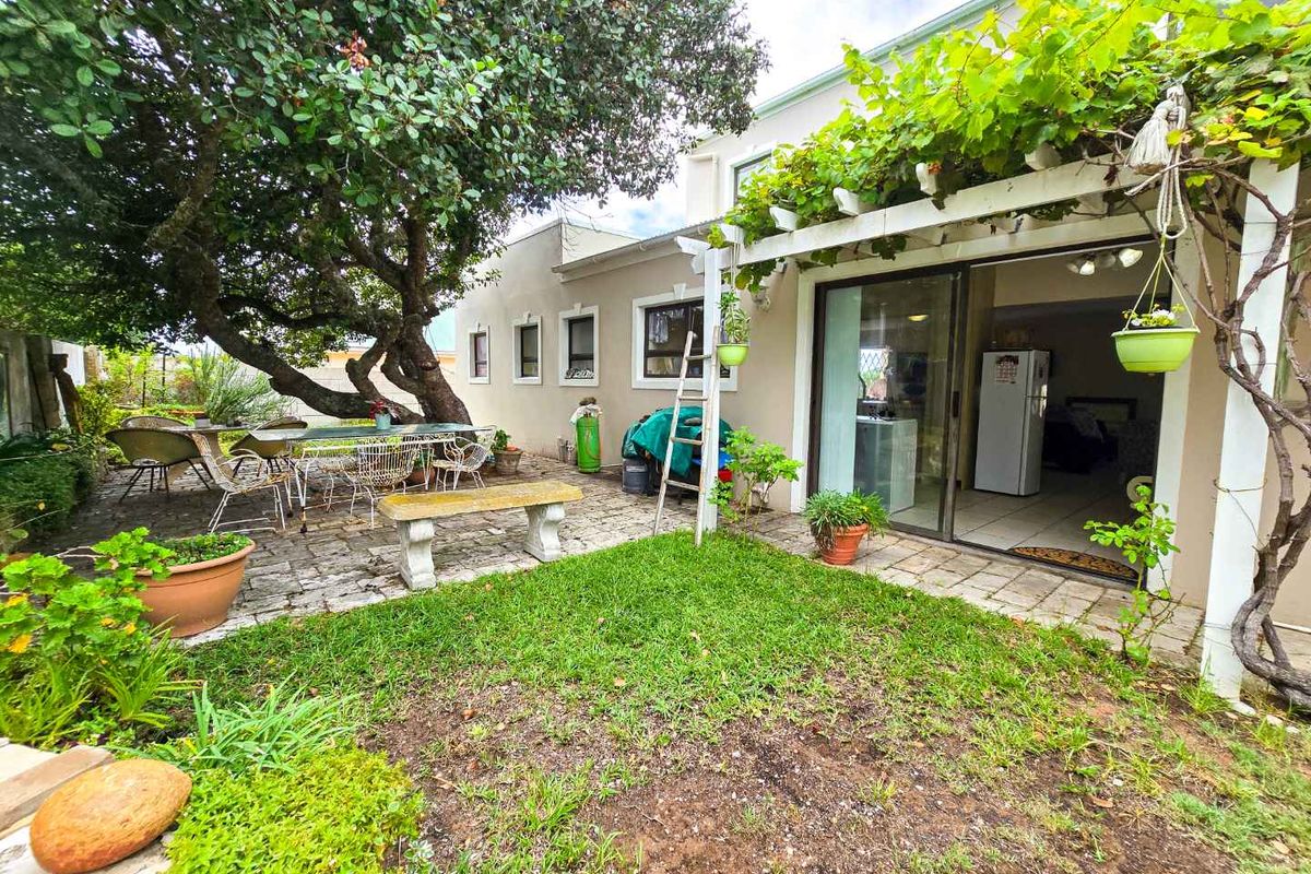 A rear garden area featuring a paved patio, a wooden pergola with climbing vines, and direct access to the interior living space via sliding doors.