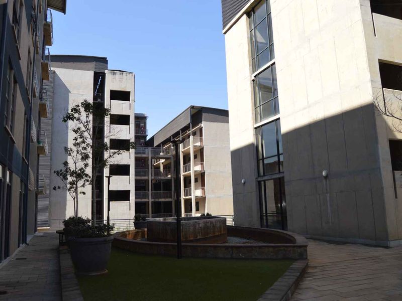 A view of the apartment complex courtyard featuring concrete building facades, a central water feature, and paved walkways between the residential blocks.