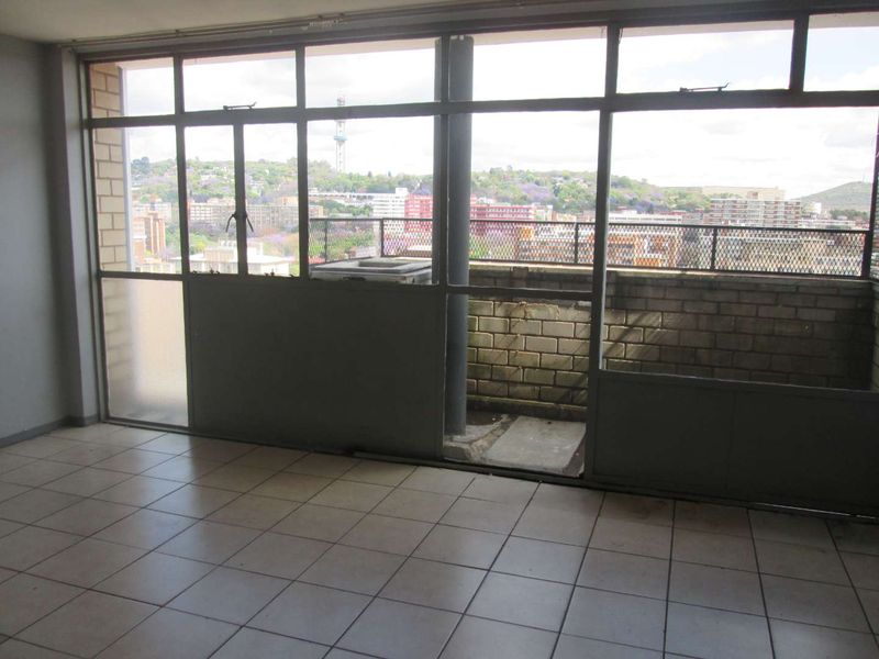 An enclosed balcony area featuring tiled flooring and large metal-framed windows with expansive urban views, offering a blank canvas for renovation.