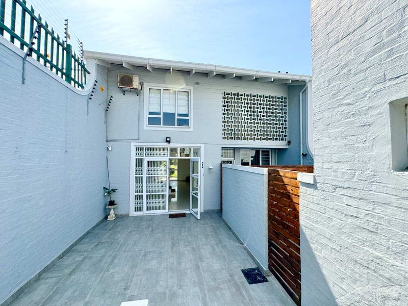 Front entrance area of the townhouse featuring a tiled patio, security gate, and decorative breeze block wall with electric fencing.