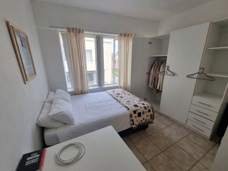 A functional bedroom featuring tiled flooring and a built-in wardrobe, offering practical storage space and natural light through the window.