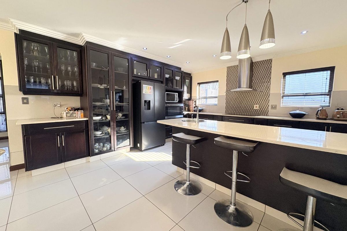 Modern kitchen featuring dark wood cabinetry, stone countertops, a central island with breakfast bar, and integrated stainless steel appliances.
