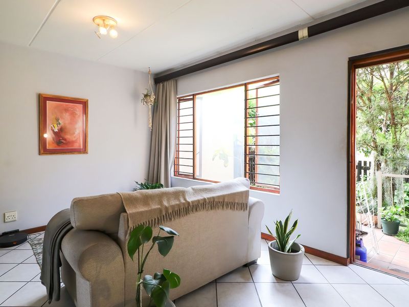 A bright living room featuring tiled flooring, security bars on the window, and direct access to an outdoor patio area.