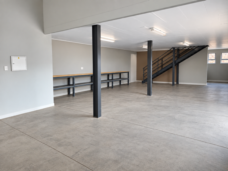 Spacious open-plan industrial unit featuring polished concrete floors, steel support columns, built-in shelving, and a metal staircase leading to an upper level.