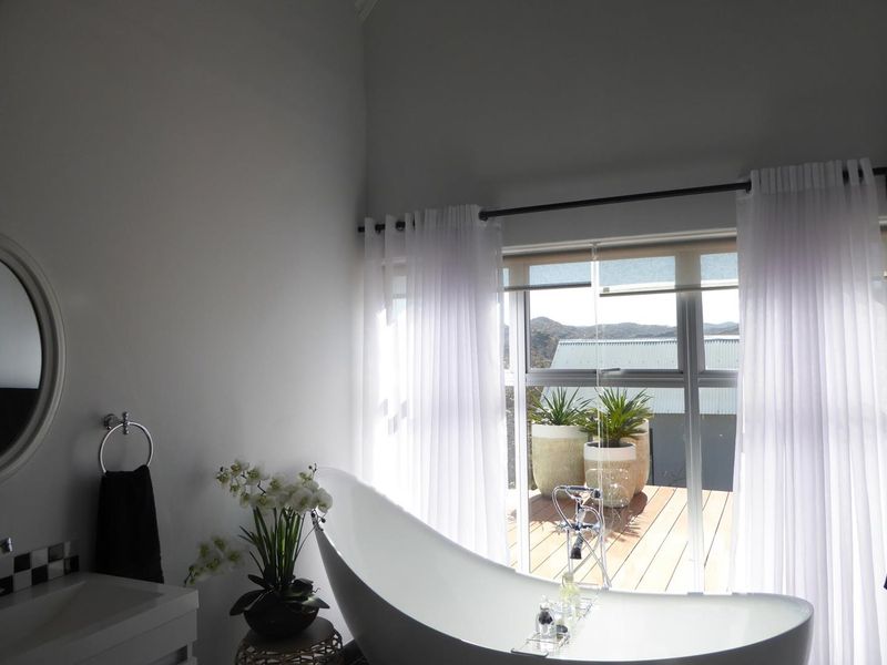 Modern bathroom featuring a sleek freestanding bathtub, vanity, and large sliding glass doors that open onto a wooden deck with scenic views.