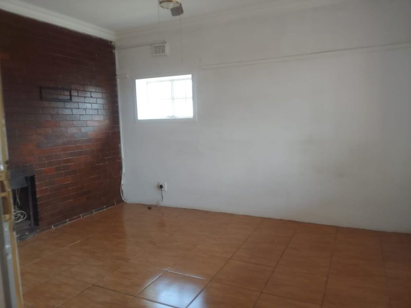 An empty living room featuring a prominent exposed brick wall with a built-in fireplace and ceramic tiled flooring.