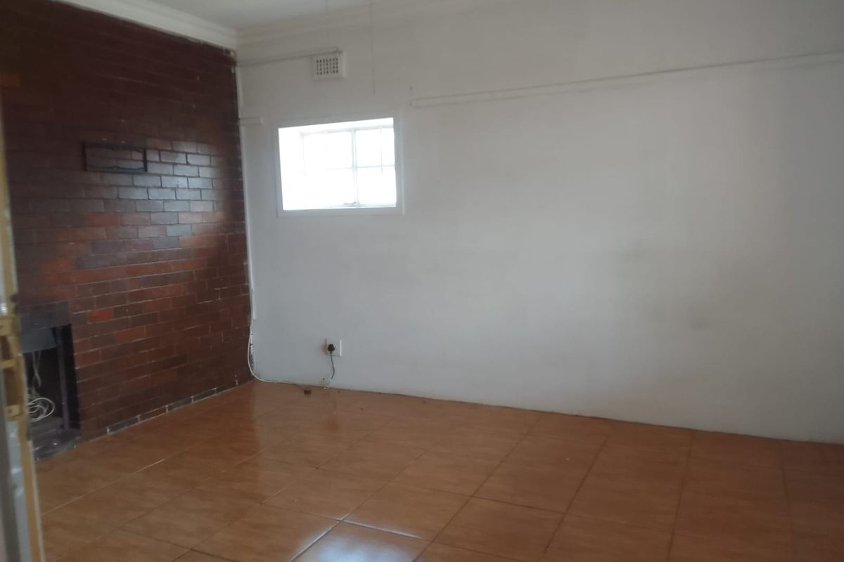 An empty living room featuring a prominent exposed brick wall with a built-in fireplace and ceramic tiled flooring.