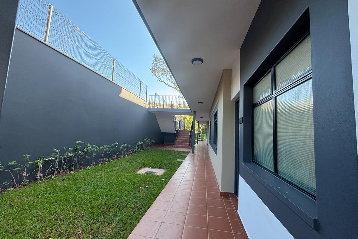 A well-maintained exterior walkway featuring tiled flooring, adjacent to a private lawn area with perimeter fencing and external staircase access.