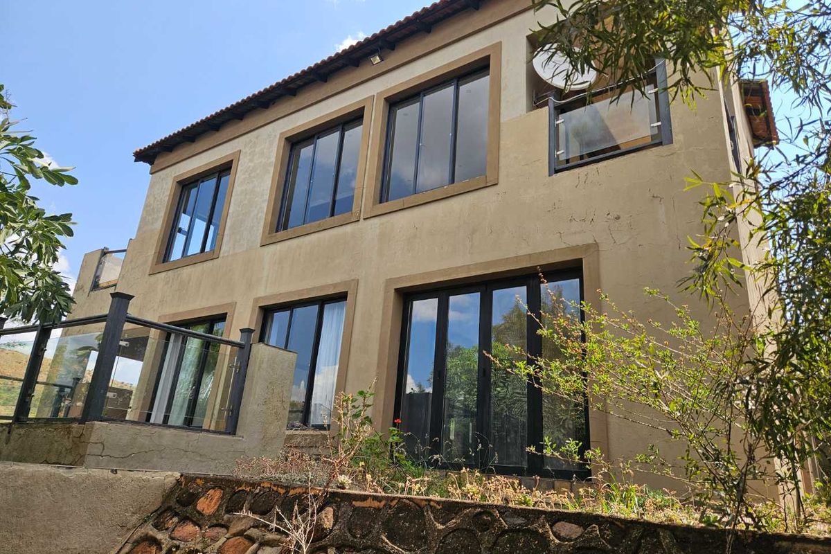 Rear elevation of a two-story house featuring large aluminium windows, glass balustrades, and a stone retaining wall in the garden area.