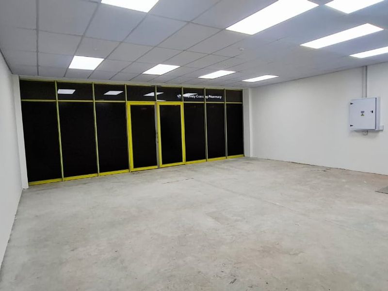 An open-plan commercial space featuring a suspended ceiling, recessed lighting, large glass storefront, and a small kitchenette area, suitable for retail or office use.